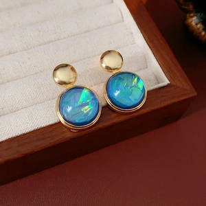 Detail of round gold resin earrings with iridescent blue stones on a wooden tray