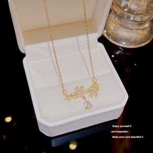 Close-up of a golden necklace with floral zircon charms and a pear-cut drop in a white box