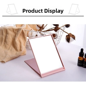 Close-up of a pink portable folding makeup mirror with adjustable stand on a white desk