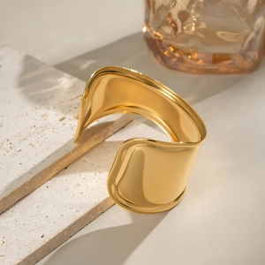Close-up of polished 18K gold plated wide wave cuff bracelet on a stone surface