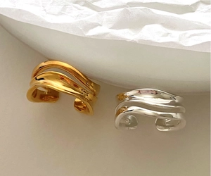 Close-up of wavy 925 sterling silver rings in gold and silver on a minimalist background