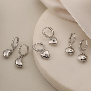 Dettaglio di tre paia di orecchini a cerchio in argento con ciondoli a cuore e disco