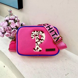 Detailed close-up of pink shoulder bag featuring blue trim and a branded logo plaque