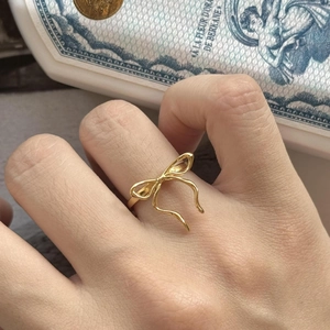 Detailed view of a dainty gold bow ring featuring a polished ribbon design on a finger