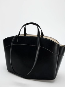 Close-up of black leather tote bag with elegant white contrast stitching and dual handles
