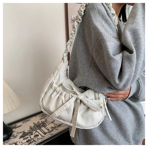 Detail of off-white pleated shoulder bag featuring a decorative bow and ruched strap