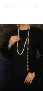 Elegante collana lunga di perle con ciondolo a fiore dorato indossata su abito nero
