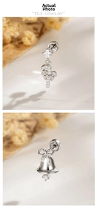 Detail of silver Christmas tree bell earrings with bows and zircon inlays on soft background