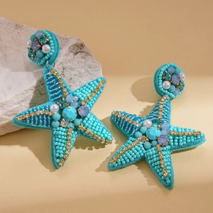 Detail of turquoise starfish earrings with pearls and rhinestones on stone background