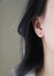 Close-up of a minimalist silver stud earring with a yellow round-cut claw-set gemstone