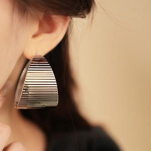 Close-up of a model wearing large textured gold geometric earrings with horizontal ridges