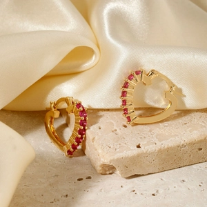 Elegant gold heart earrings with ruby red stones on silk and stone background