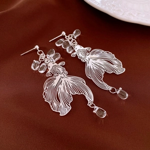 Detail shot of hollow silver koi fish earrings with elegant flowing tail and glass beads