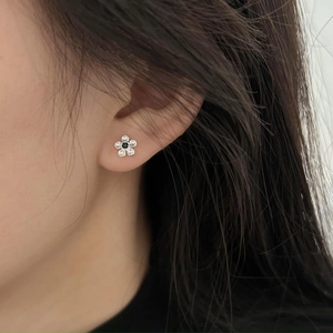 Close-up of a silver flower stud earring with black and white crystals on a female ear