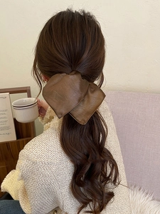 Detail of dark brown leather bow hair scrunchie worn on a ponytail in soft indoor light