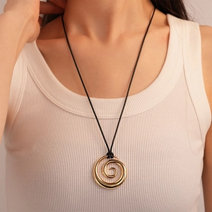 Close-up of golden spiral swirl pendant necklace on black cord worn by a model