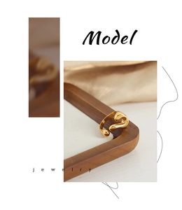 Artistic close-up of a gold-toned fluid geometric open ring on a wooden tray with silk