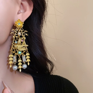 Detailed shot of vintage gold bird earrings with colorful gemstones and pearls on model