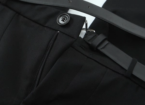 Close-up of black twill trousers waist area with button, zipper and leather belt detail