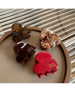 Detail of four heart-shaped acetate hair claws in tortoise and red on a leather tray