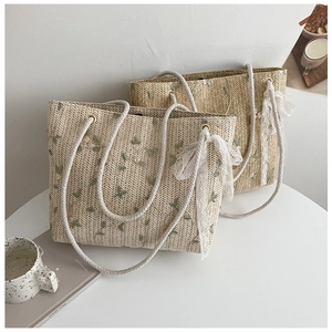 Detail of straw woven tote bag featuring green floral embroidery and white lace ribbon