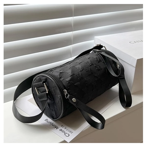 Detail of black cylindrical crossbody bag featuring pleated texture and wide shoulder strap