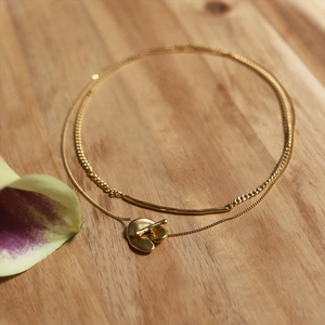 Golden double-layer brass necklace with a minimalist geometric pendant on a wooden surface