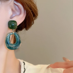 Close-up of resin earrings featuring green marble texture and geometric rhombus shapes