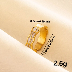 Détail d'une bague dorée avec texture émail blanc sur fond de soie beige