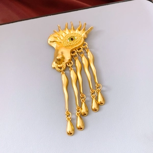 Macro view of vintage gold surrealist eye brooch with green pupil and wavy fringe drops