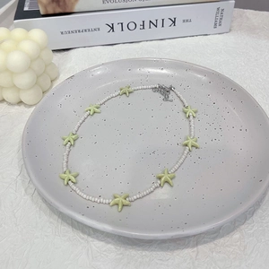 Close-up of white seed bead necklace with light green starfish pendants on a ceramic tray