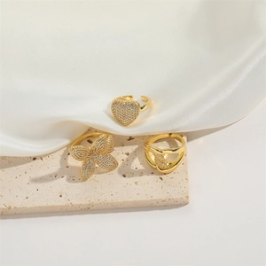 Close-up of gold heart and butterfly rings with cubic zirconia on a beige stone surface