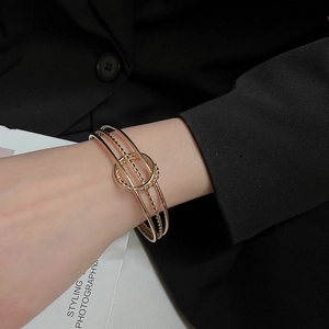 Detail of layered gold twisted metal cuff bracelet worn with a stylish black blazer