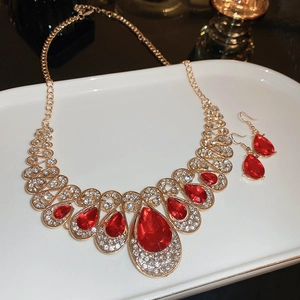 Detailed set of golden teardrop necklace and earrings with red gems on white ceramic plate