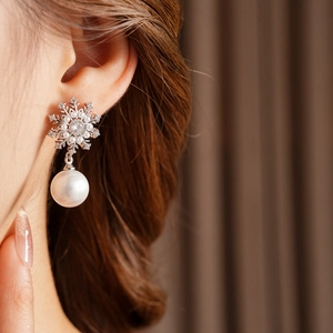Gros plan sur boucle d'oreille flocon argentée avec zircon et perle pendante