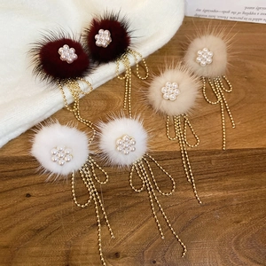 Close-up of fluffy fur flower earrings with long pearl tassels on a cozy winter backdrop