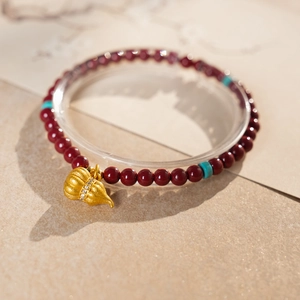 Macro detail of cinnabar beaded bracelet with gold gourd pendant and turquoise accents