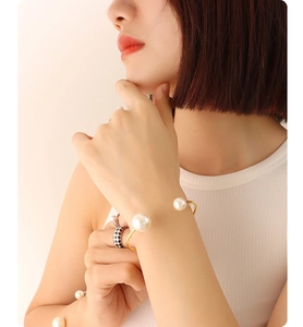 Detail of elegant gold-plated open bangle with white pearls and checkerboard ring on model
