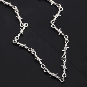 Detailed view of silver gothic barbed wire necklace with heart rose motif on black background