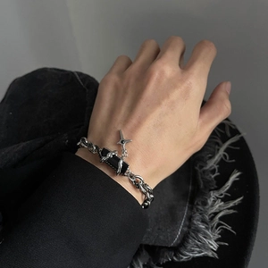 Close-up of a silver chain bracelet with a black gemstone and cross charm on a wrist