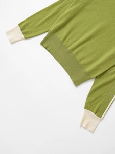 Detail of green knit sweater with contrast white ribbed hem and cuffs on white backdrop