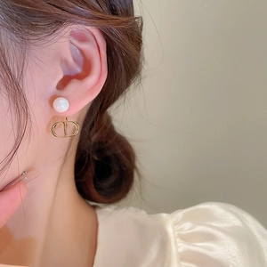 Close-up of gold CD letter drop earrings with white pearls in a minimalist luxury style