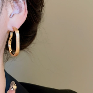 Close-up of a matte gold twisted geometric hoop earring worn by a female model