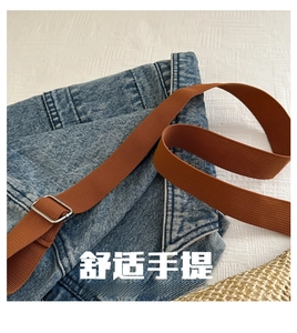Close-up of denim sling bag with brown fabric shoulder strap and silver metal buckle