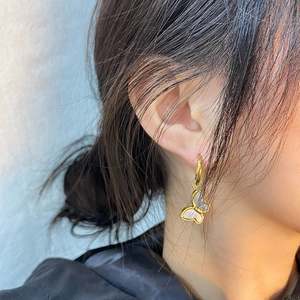 Close-up of a model wearing a gold butterfly earring with white shell inlay
