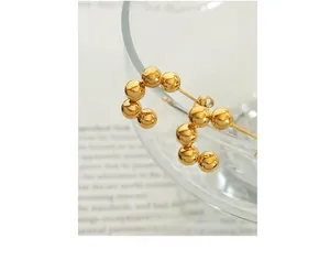 Macro shot of 18k gold plated C-shaped bead earrings hanging on a glass rim