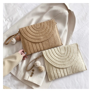 Detail of hand-woven straw envelope bags with decorative pom-poms and wrist straps