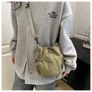 Detail of olive green nylon drawstring crossbody bag with side mesh pocket on model