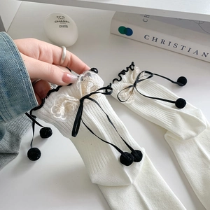 Detail of white rib-knit socks with black ruffle trim and delicate lace bow accents
