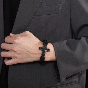 Men's braided leather bracelet with stainless steel cross charm on a suited model